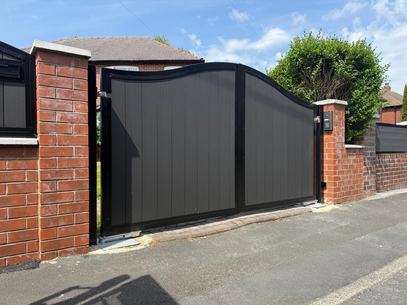 Elegant curved-top double driveway gates in dark grey steel with vertical plank design and keypad entry system, installed by Colemans Steel Leeds